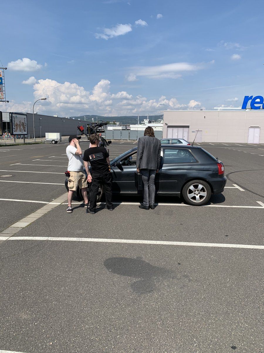 Zwei Crew-Mitglieder filmen Herrn Grau vor seinem Auto.